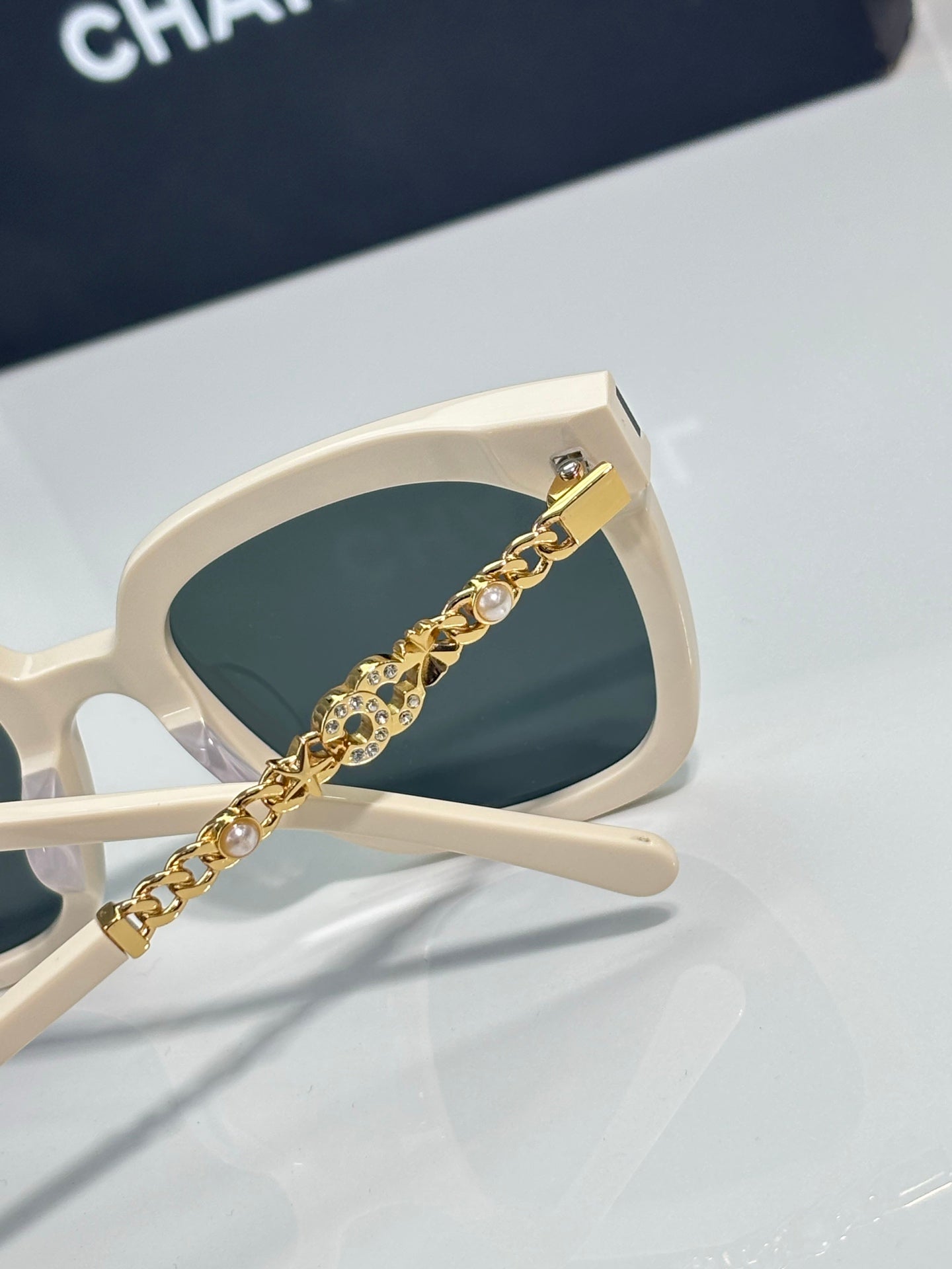 Chanel sunglasses close-up with white frame and gold chain pearl detail on arm