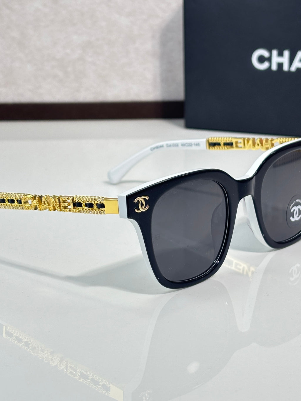 Chanel sunglasses side view with black lens, dark frame, and white temple with gold trim