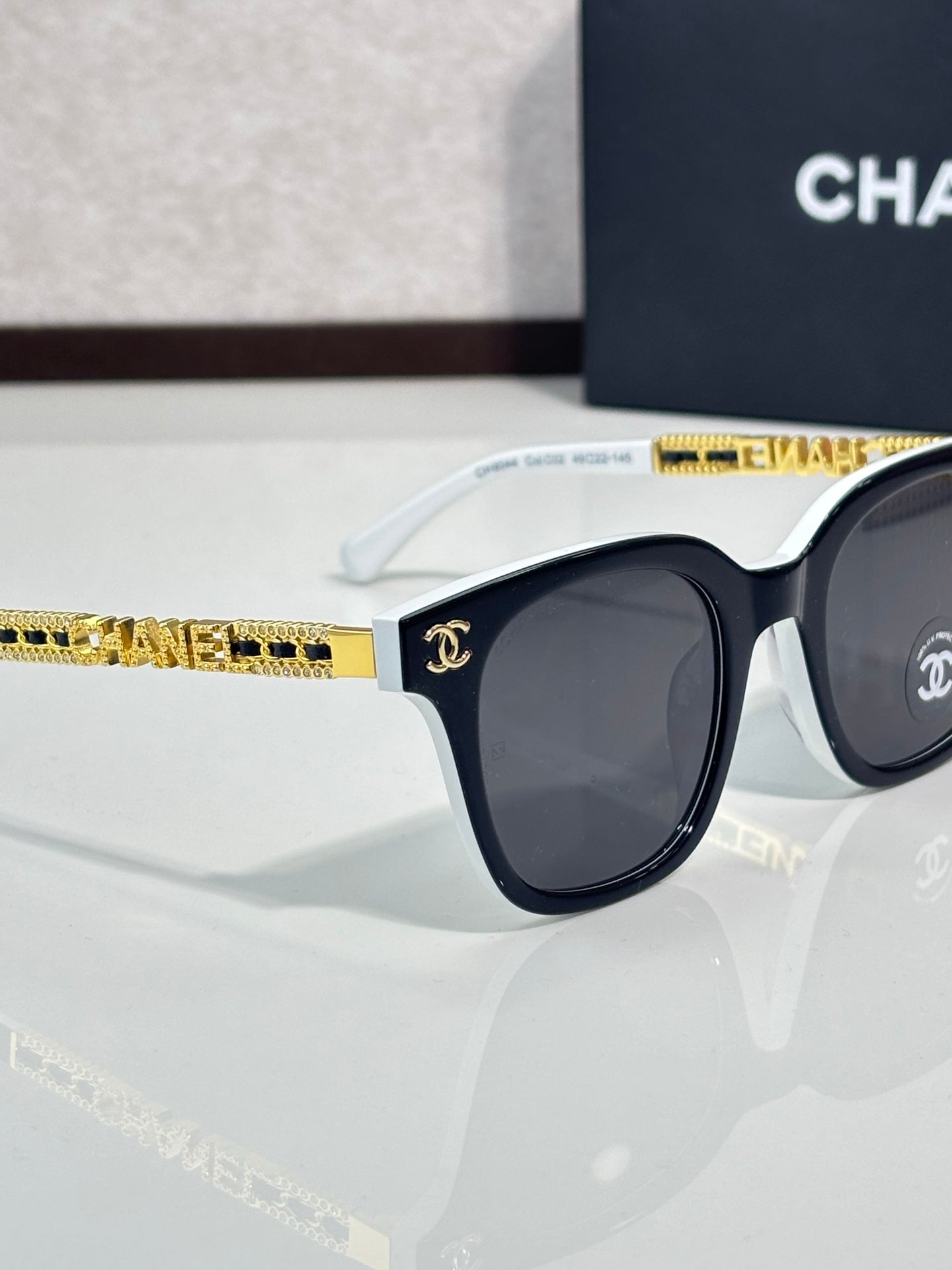 Chanel sunglasses side view with black lens, dark frame, and white temple with gold trim