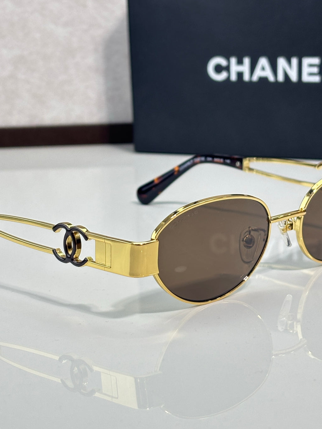 Round sunglasses with gold frame and brown-tinted lenses, side temple logo detail