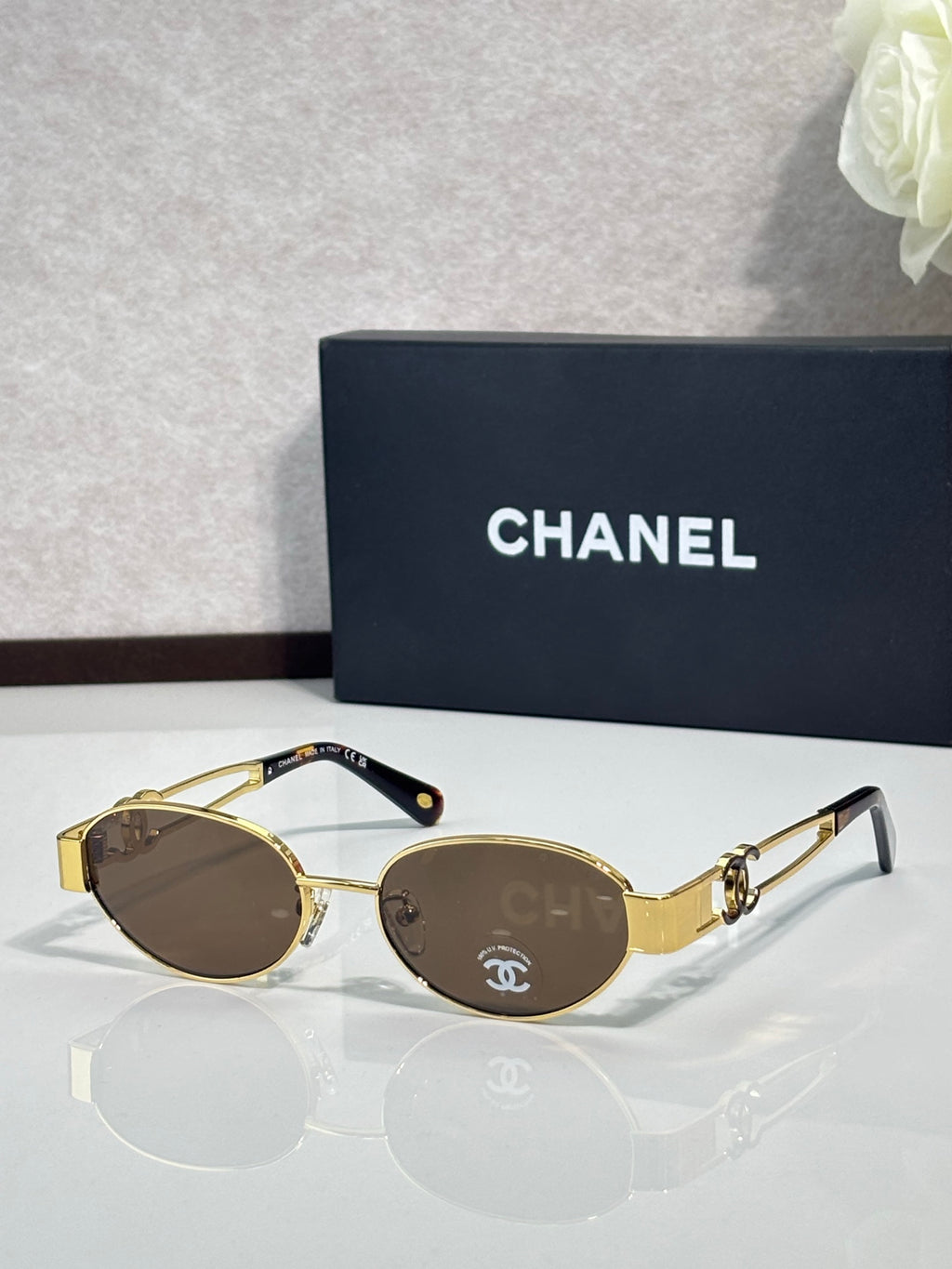 Round sunglasses with gold frame and brown-tinted lenses, logo detail on temple