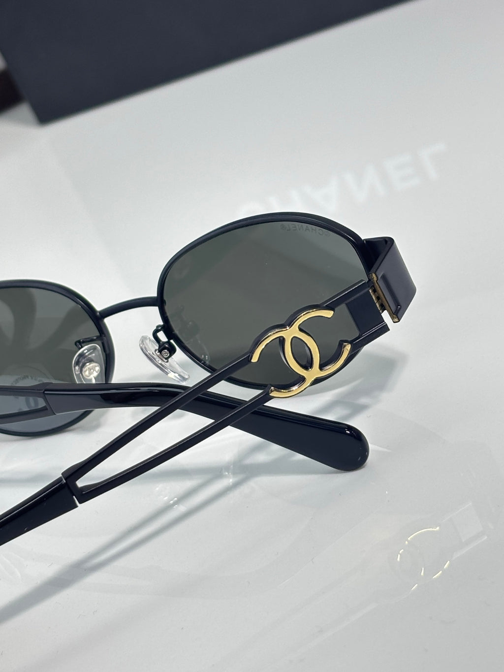 Round sunglasses with dark navy frame and dark lenses, gold logo detail on temple
