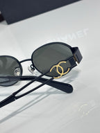 Round sunglasses with dark navy frame and dark lenses, gold logo detail on temple