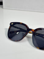 Tortoiseshell sunglasses close-up with dark lenses and gold-tone logo bar on temple