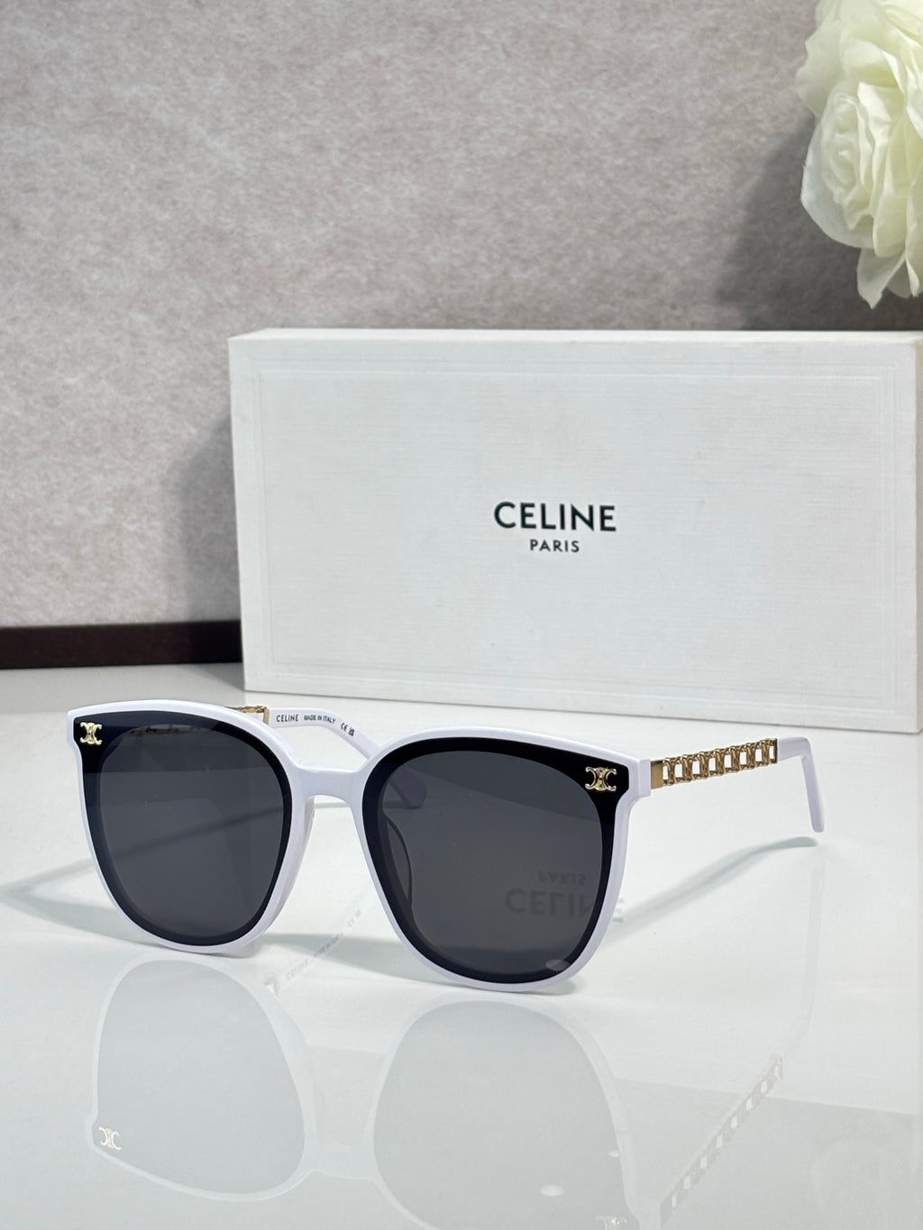 Sunglasses with pale white frames and dark lenses, gold-tone logo accents on temples