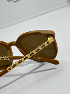 Sunglasses temple detail with gold-tone logo studs and dark lenses on tortoiseshell