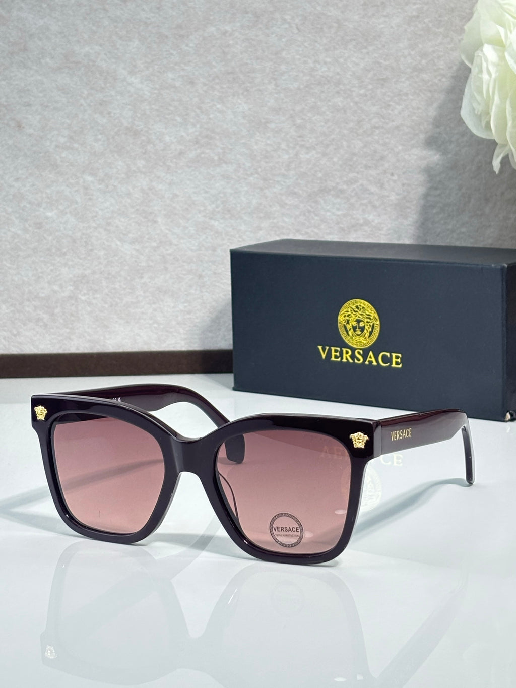 Versace sunglasses with black square frames and rose-tinted lenses, gold logo on temple