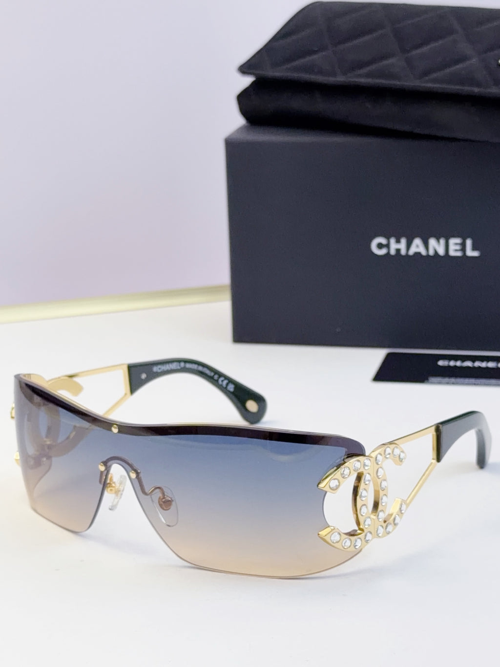 Sunglasses with light blue gradient lenses and gold-tone frame, rhinestone CC-style emblem
