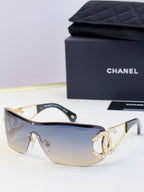 Sunglasses with light blue gradient lenses and gold-tone frame, rhinestone CC-style emblem