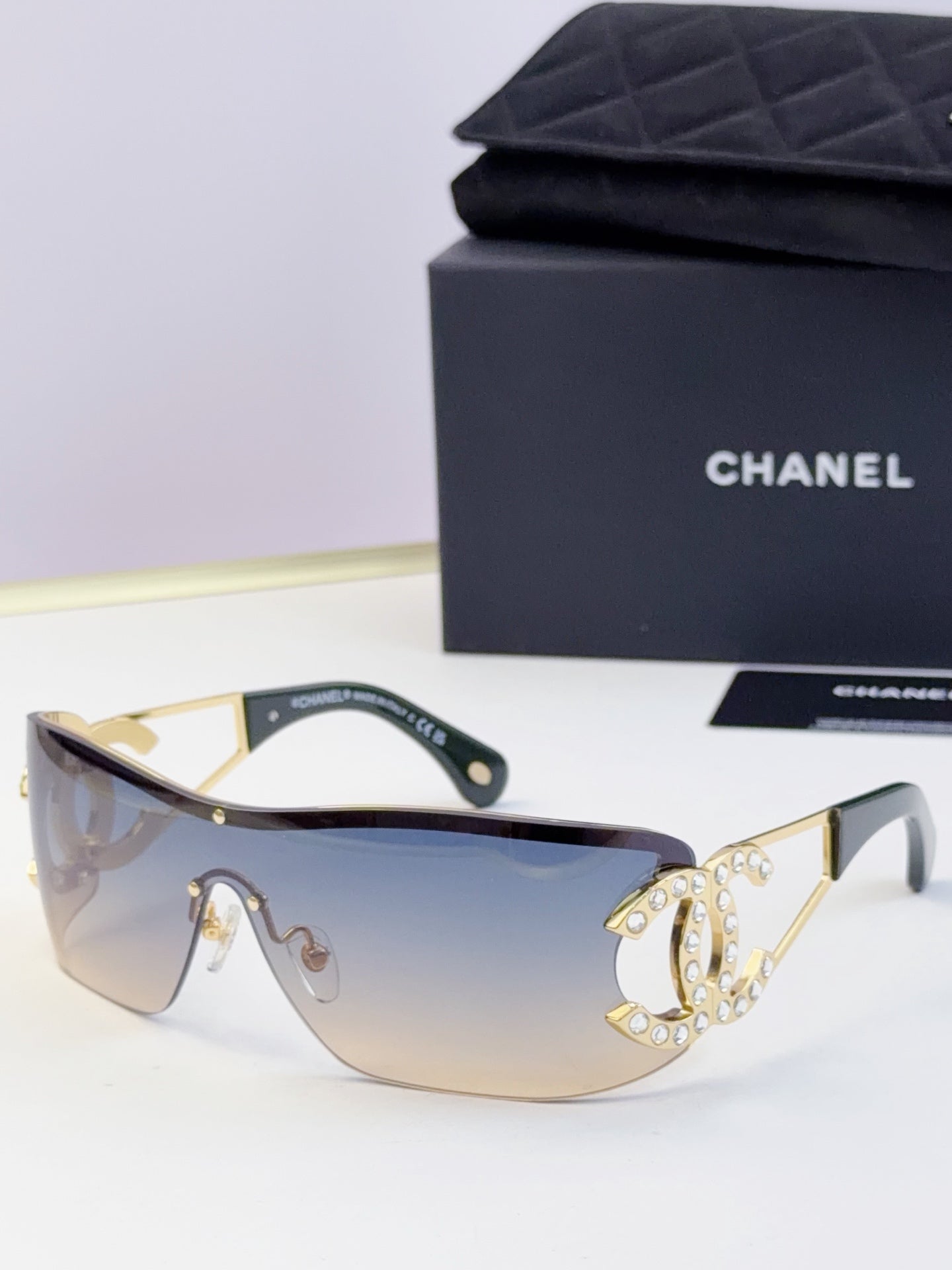 Sunglasses with light blue gradient lenses and gold-tone frame, rhinestone CC-style emblem