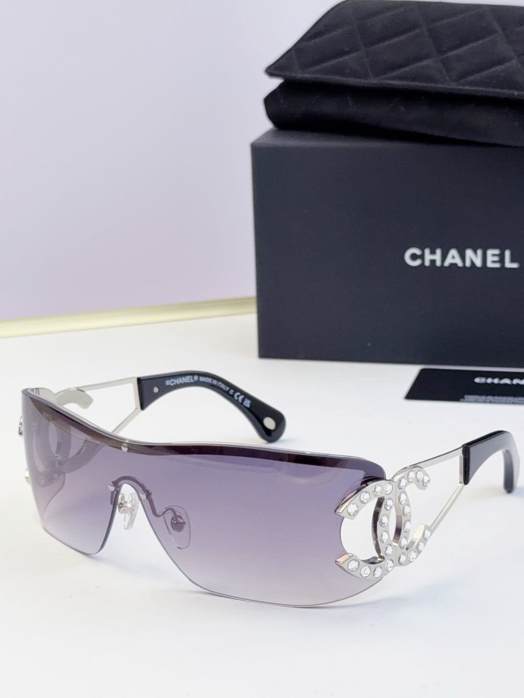 Sunglasses with lavender-blue lenses and gold-tone frame, rhinestone CC-style emblem