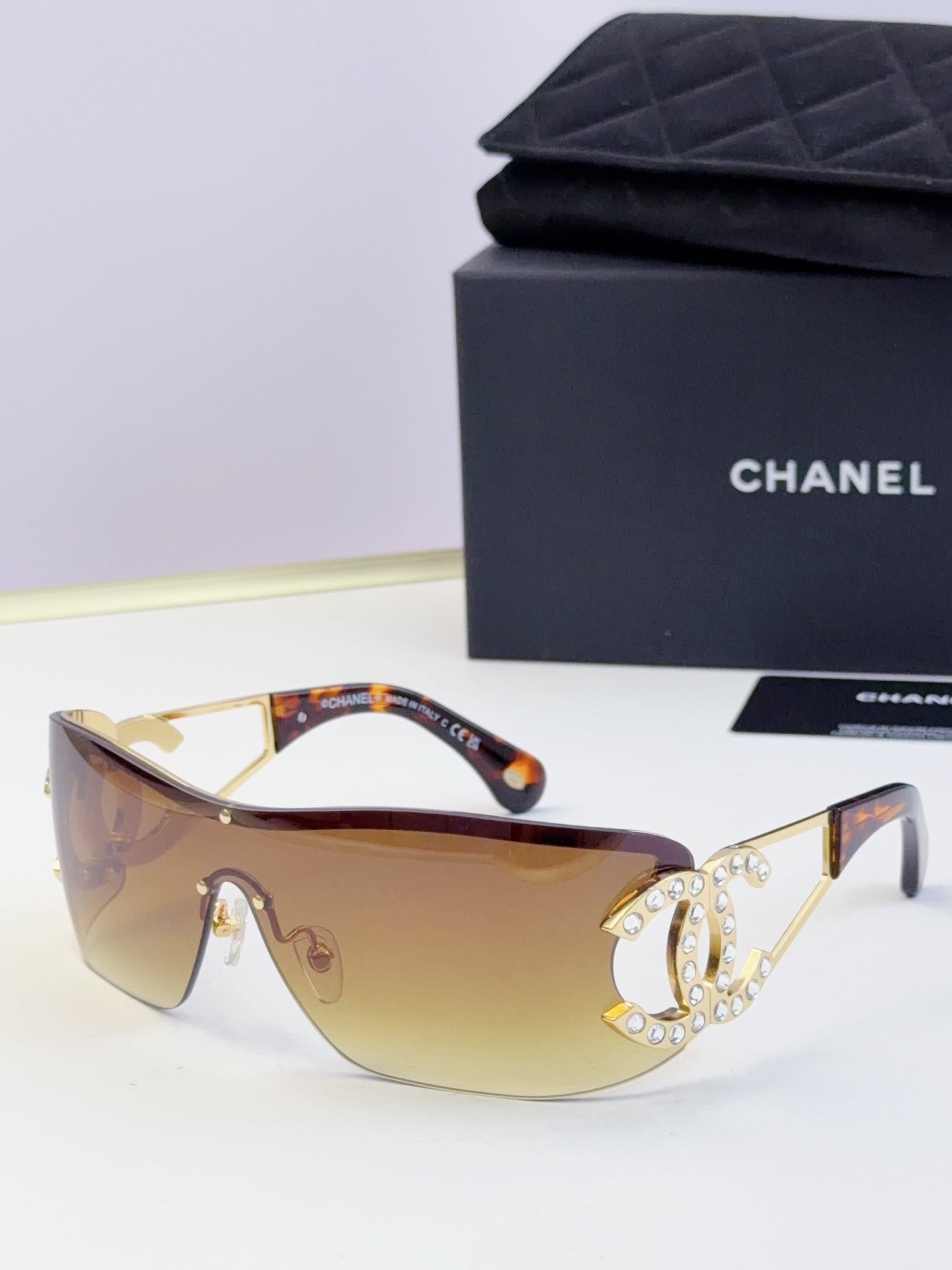 Sunglasses with amber gradient lenses and gold-tone frame, rhinestone CC-style emblem