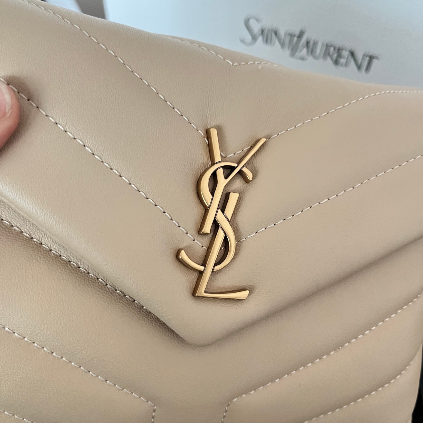 Beige YSL flap bag close-up of gold YSL logo on quilted front