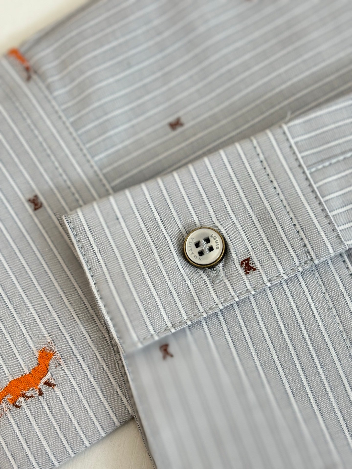 Close-up of light blue striped collar and button with orange dog embroidery