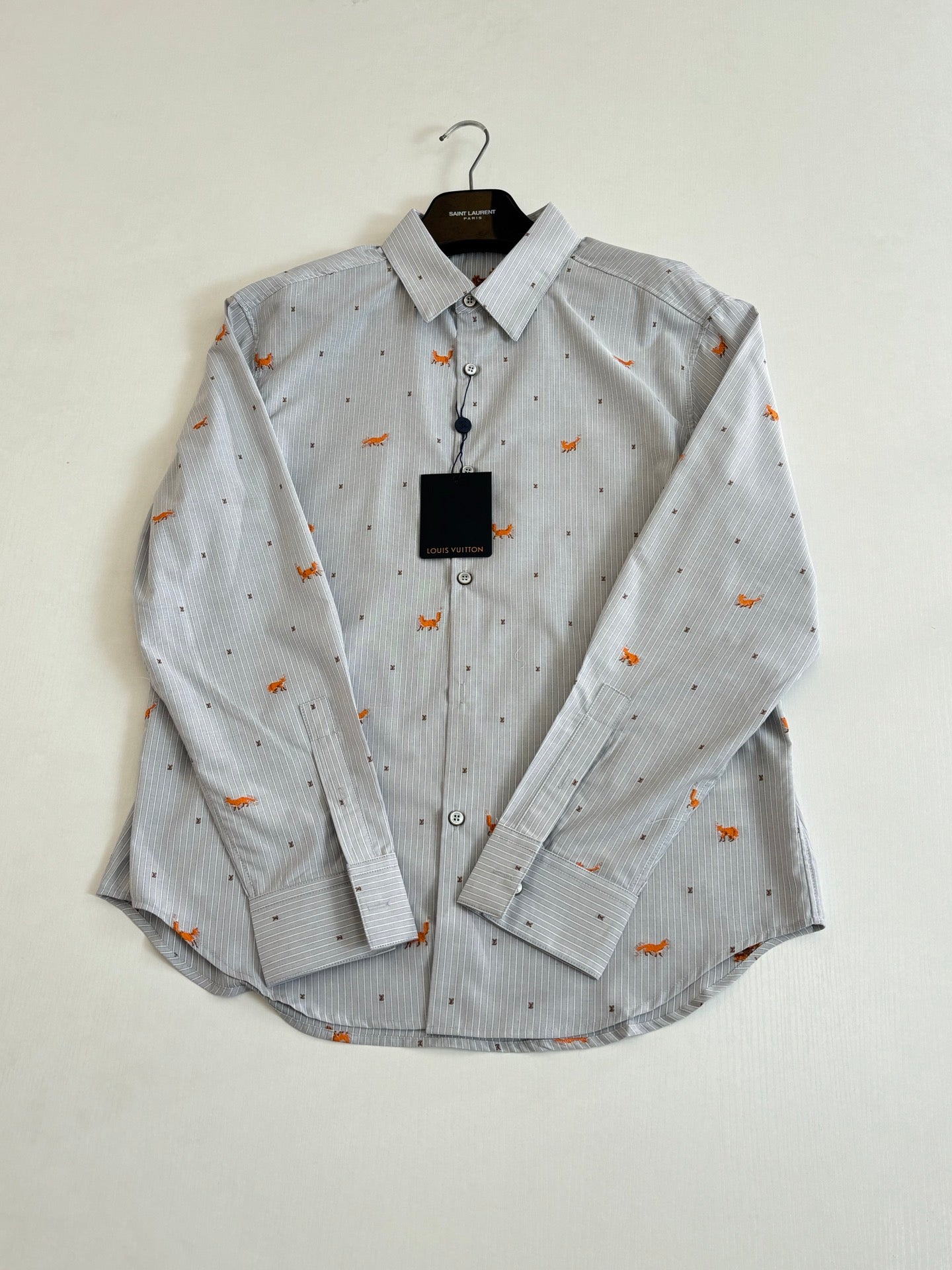 Light blue striped button-up shirt with orange dog embroidery, front view on hanger