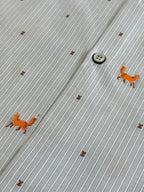 Close-up of light blue striped fabric with small orange dog embroidery and button