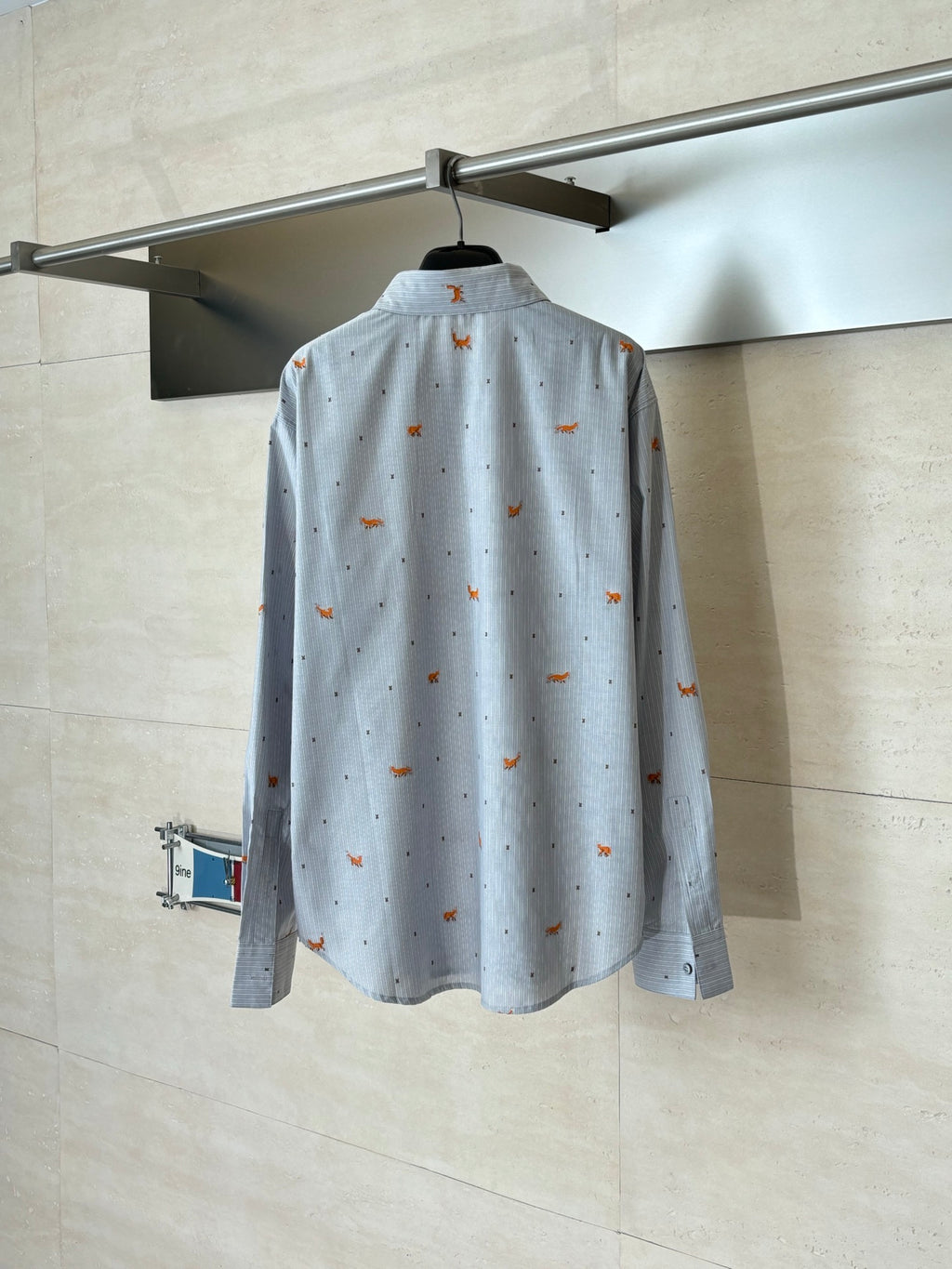 Light blue long-sleeve button-up shirt with orange dog embroidery, back view on hanger