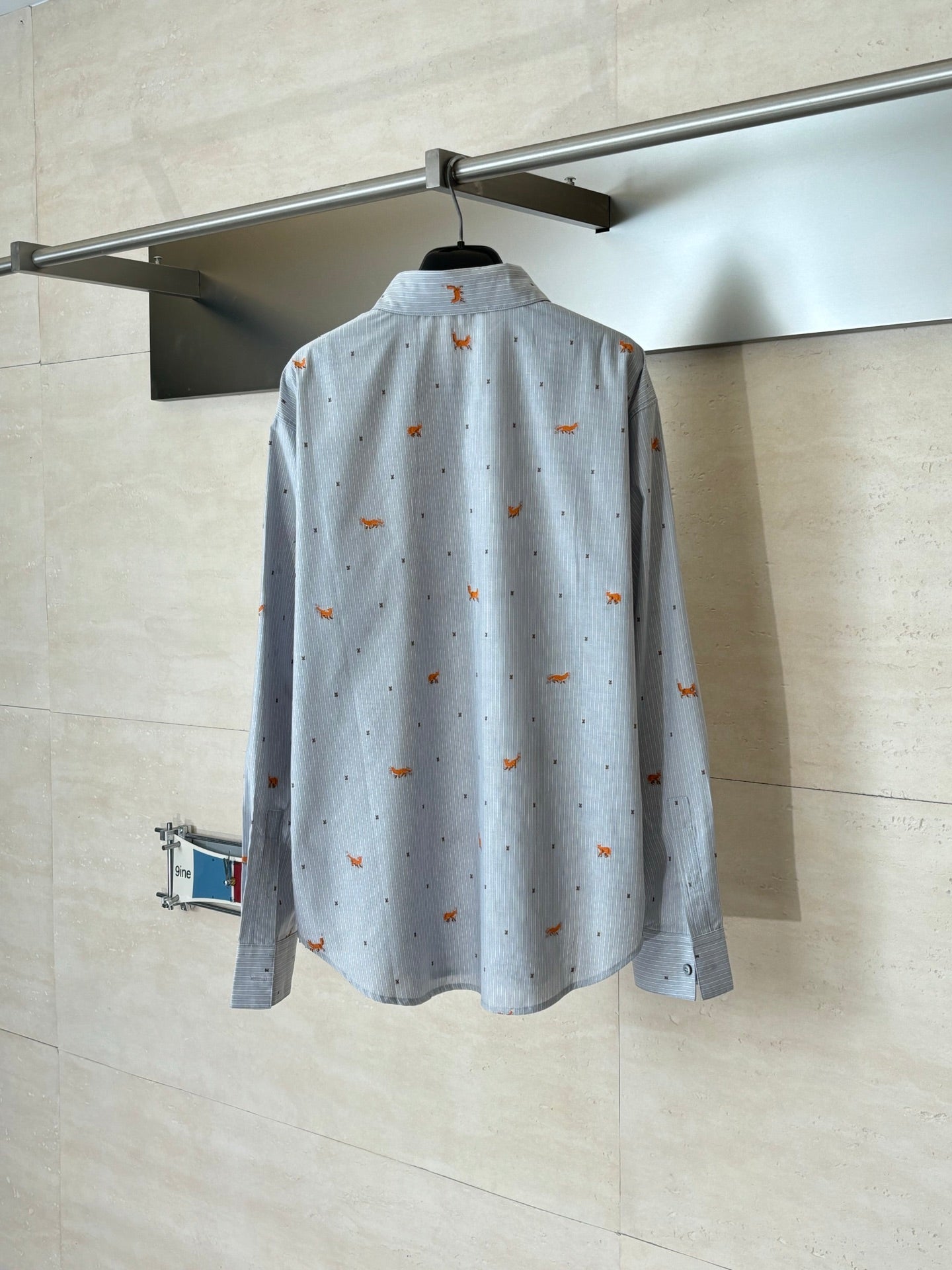 Light blue long-sleeve button-up shirt with orange dog embroidery, back view on hanger