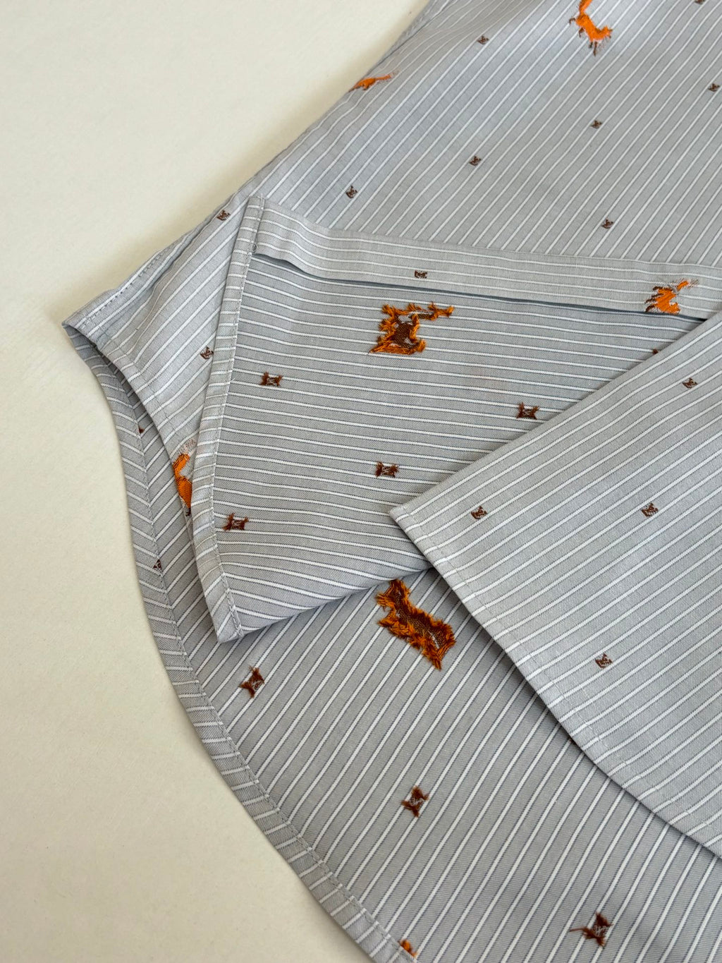 Folded light blue striped shirt with orange dog embroidery, showing collar and placket