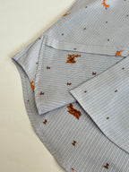 Folded light blue striped shirt with orange dog embroidery, showing collar and placket