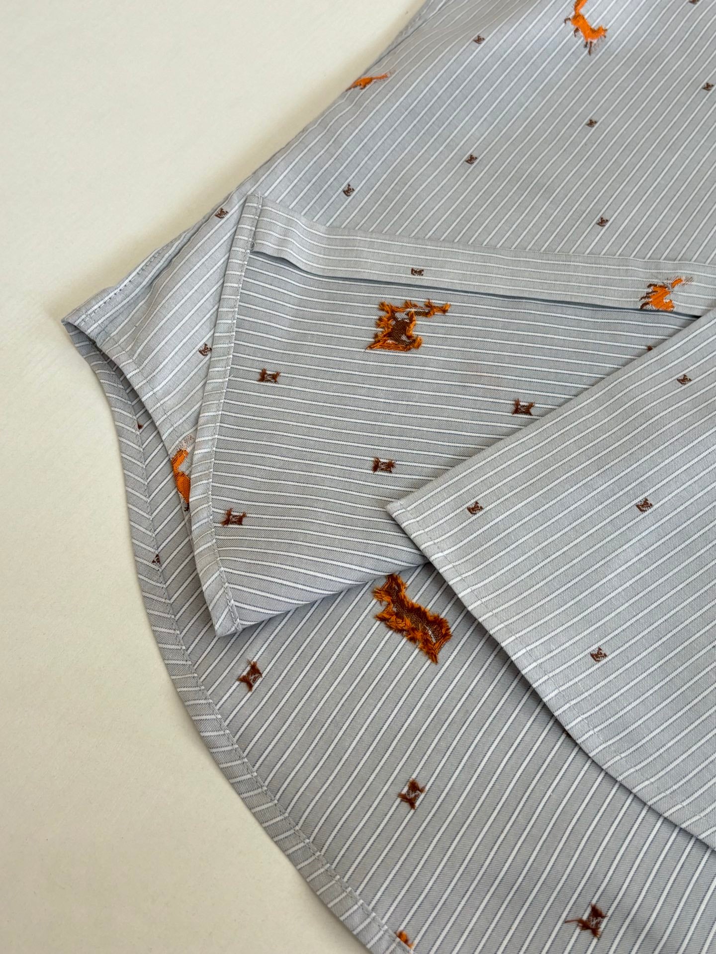 Folded light blue striped shirt with orange dog embroidery, showing collar and placket