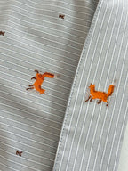 Close-up of light blue striped cuff with orange dog embroidery and stitched edge