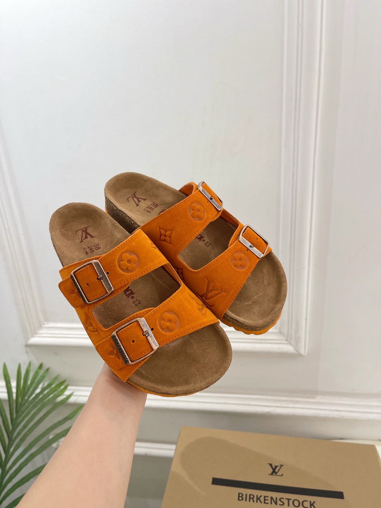 Orange Louis Vuitton sandals with double buckled straps and brown footbed, side view.
