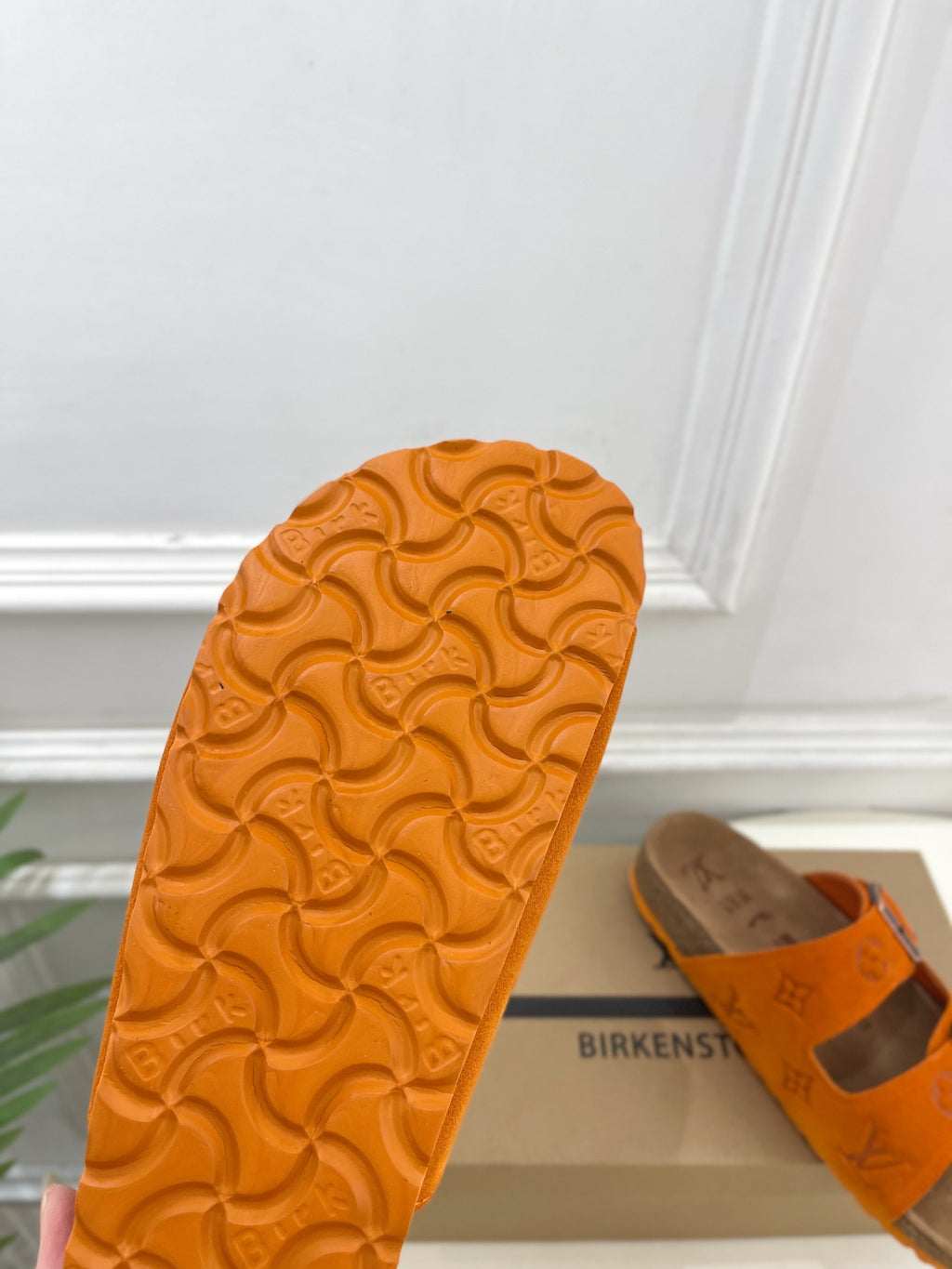 Orange Louis Vuitton sandal outsole with embossed pattern; brown strap visible.