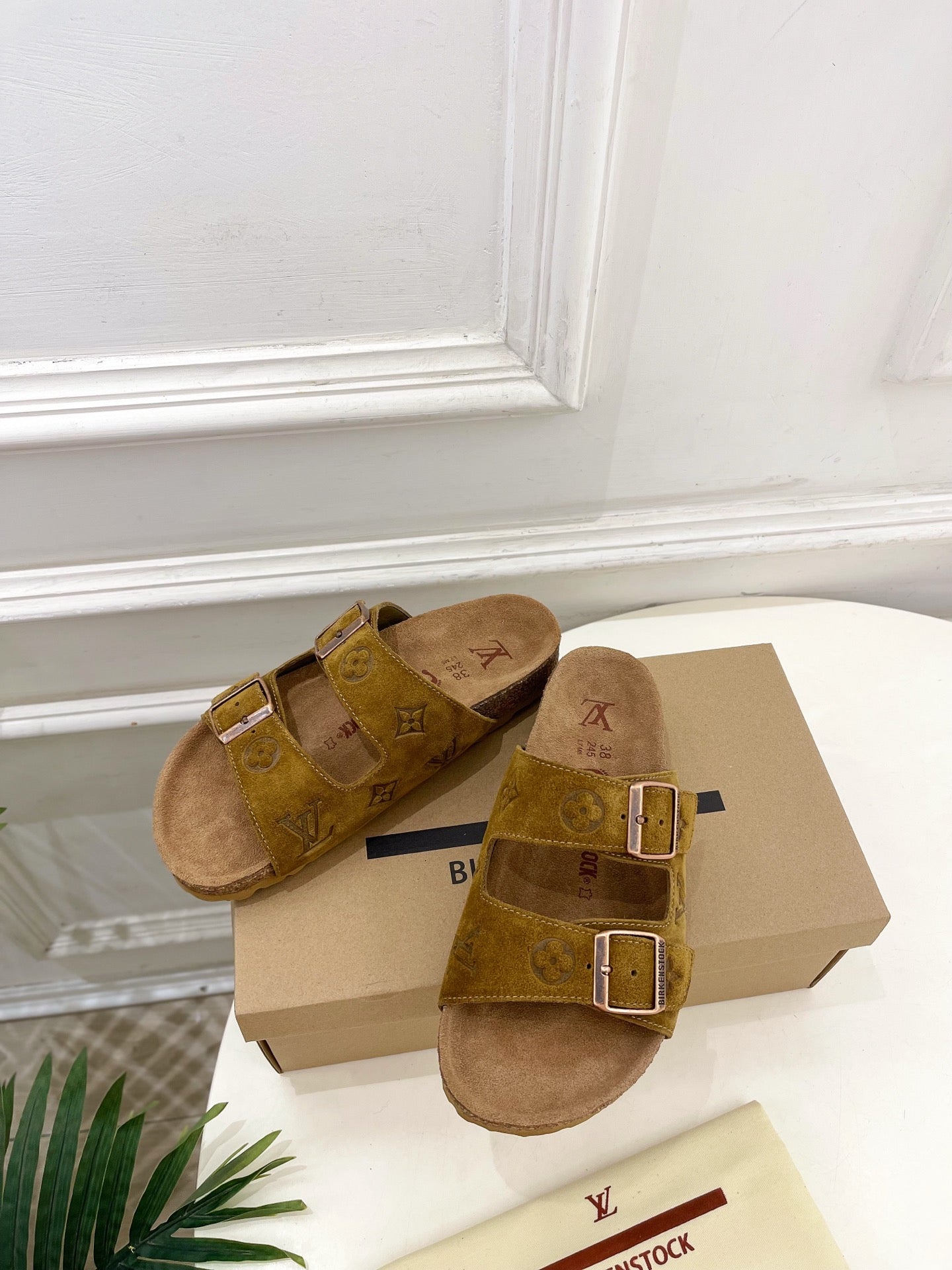 Tan monogram slide sandals with two silver-buckled straps on a tan box