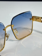Square sunglasses close-up with blue gradient lenses and gold temple hardware