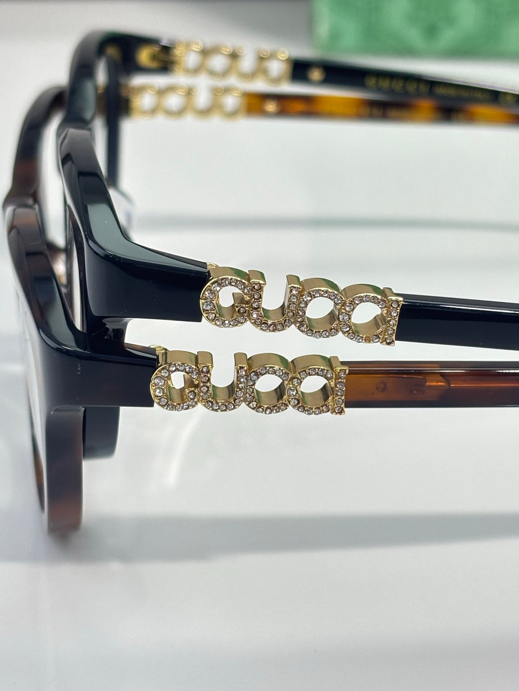 Gucci eyeglasses close-up with dark frames and gold decorative logo on bridge