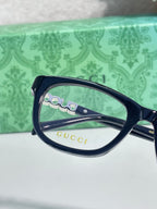 Gucci eyeglasses close-up with navy frames, clear lenses, and Gucci logo on arm
