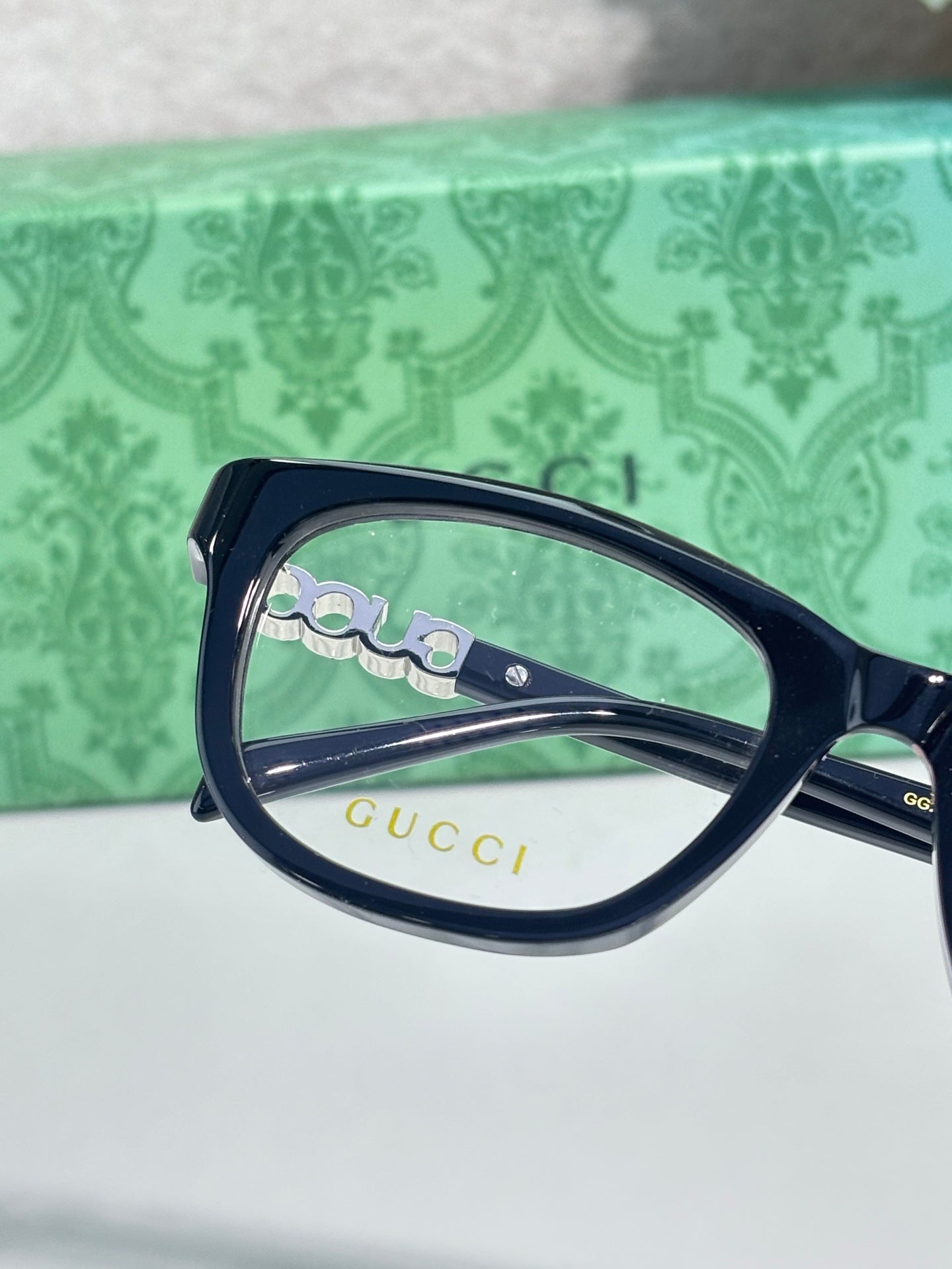Gucci eyeglasses close-up: dark navy frame with gold logo on lens and temple