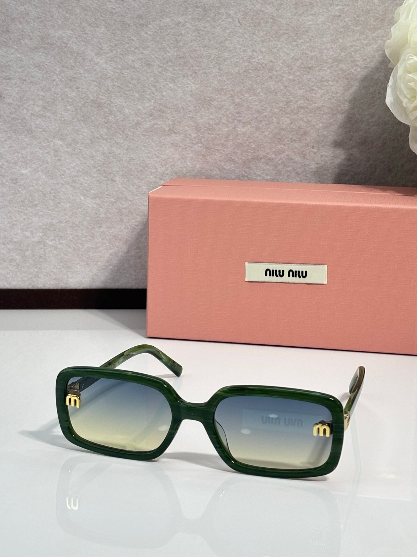 MiuMiu green sunglasses with tinted lenses and gold logo at temple