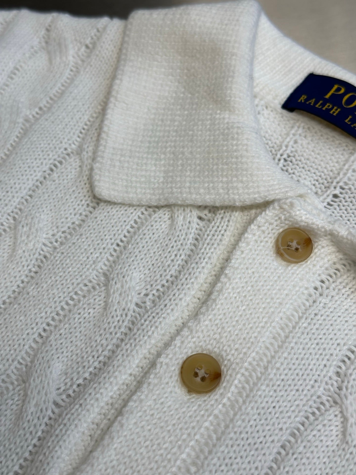 White knit polo shirt front with ribbed collar and tan button placket.