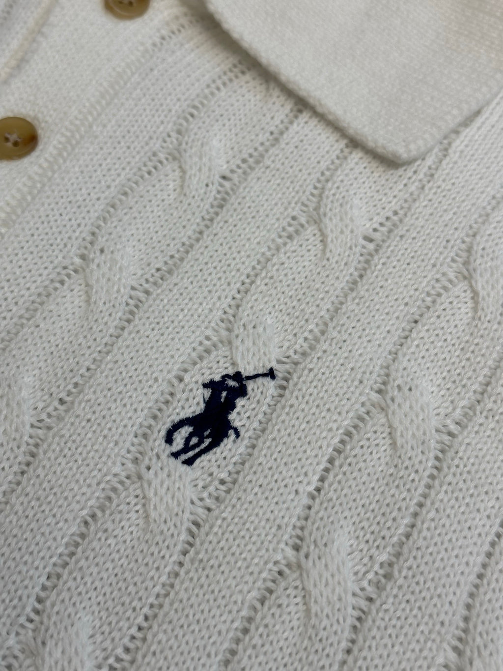 White knit polo shirt chest logo detail with cable pattern and button collar.