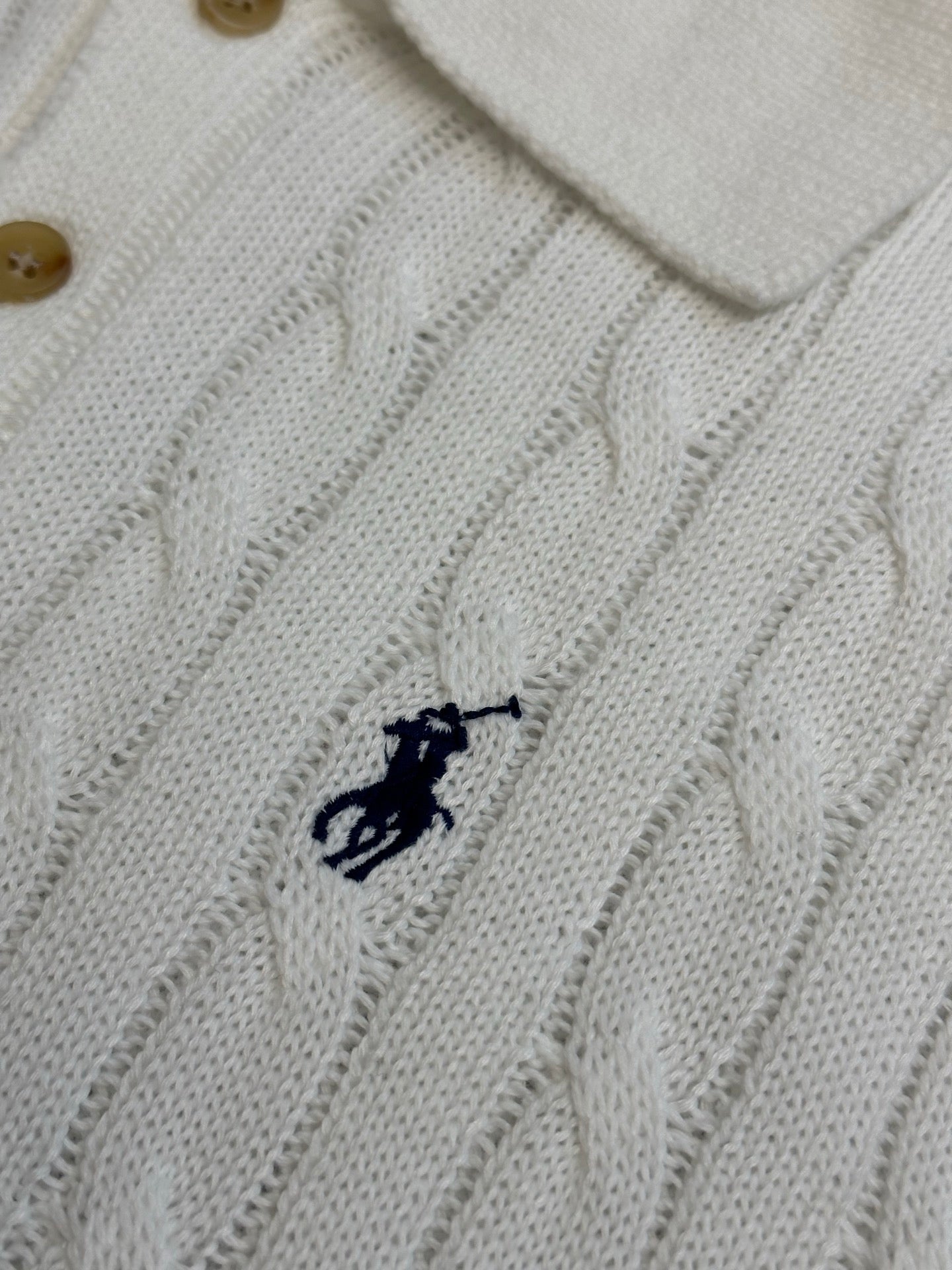 White knit polo shirt chest logo detail with cable pattern and button collar.