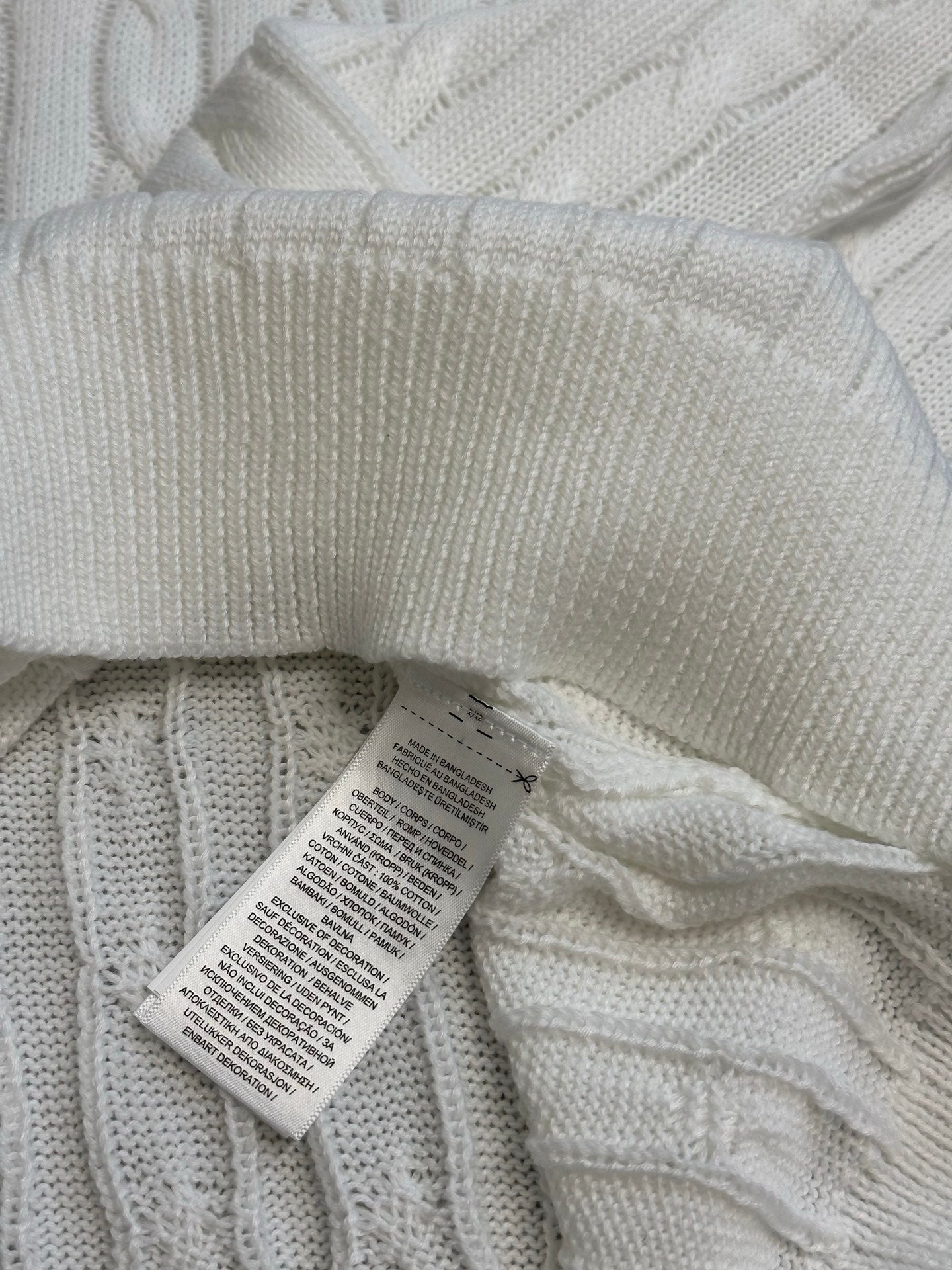 White knit polo shirt with folded fabric and attached care label tag.