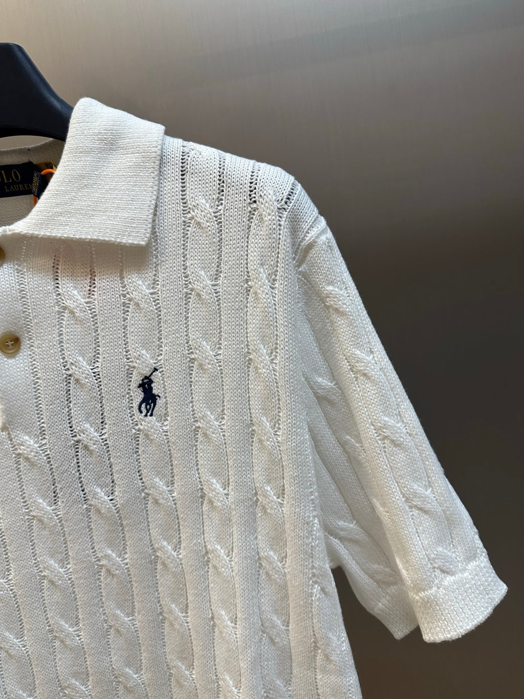 White knit polo shirt shoulder and sleeve detail with cable pattern and navy logo.
