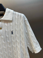 White knit polo shirt shoulder and sleeve detail with cable pattern and navy logo.