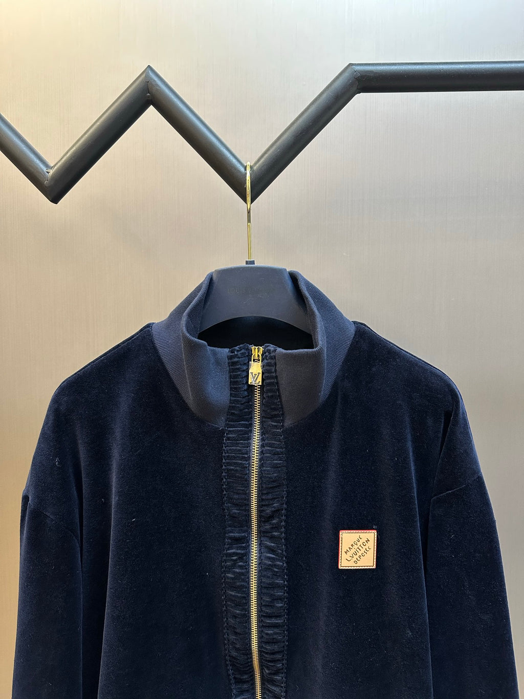 Navy zip-up jacket with stand collar, gold zipper, small logo patch on chest