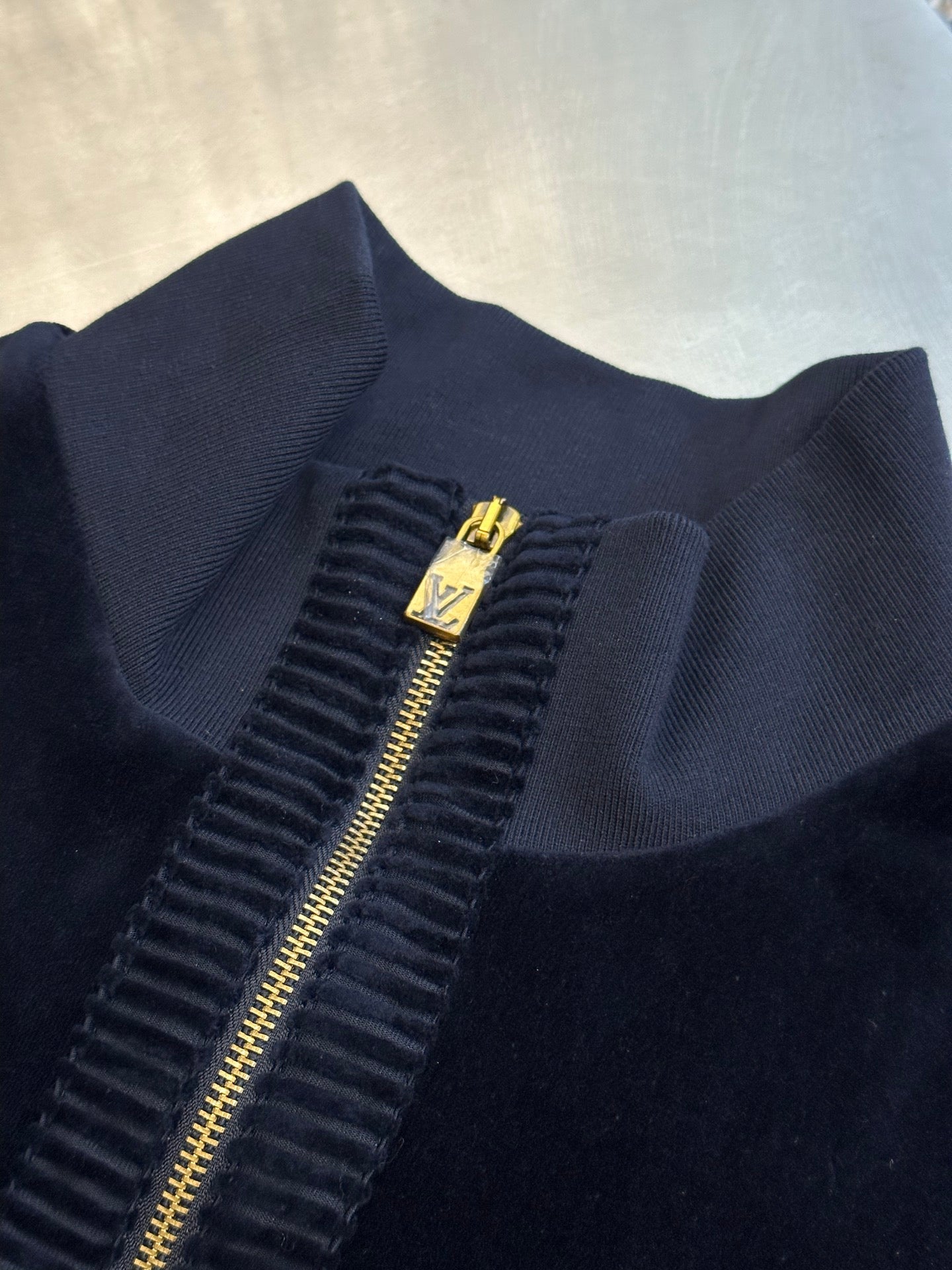 Navy jacket zipper with gold pull and small logo crest on placket