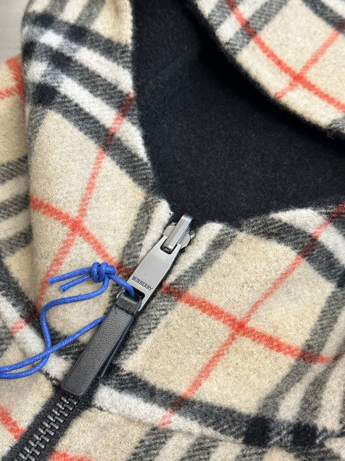 Burberry plaid fleece fabric closeup, cream with black and red grid, blue drawcord and zip