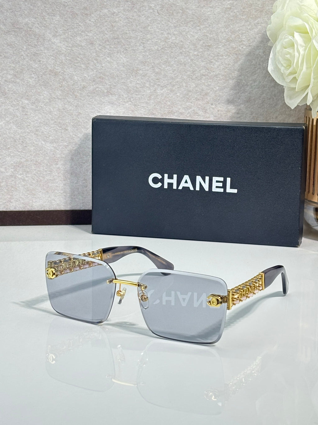 Chanel sunglasses with light gray lenses and gold chain temple accents, rectangular frames