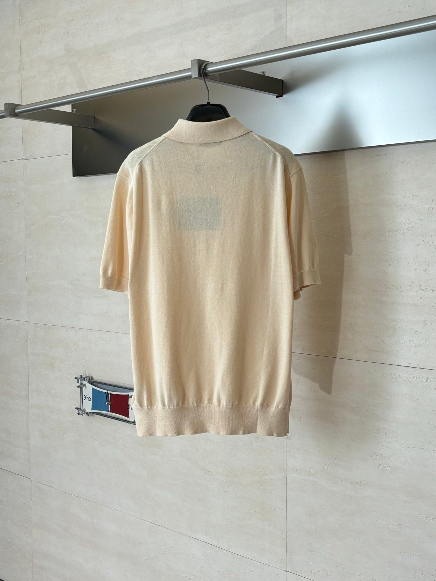 Beige short-sleeve polo shirt back view with ribbed hem on a hanger