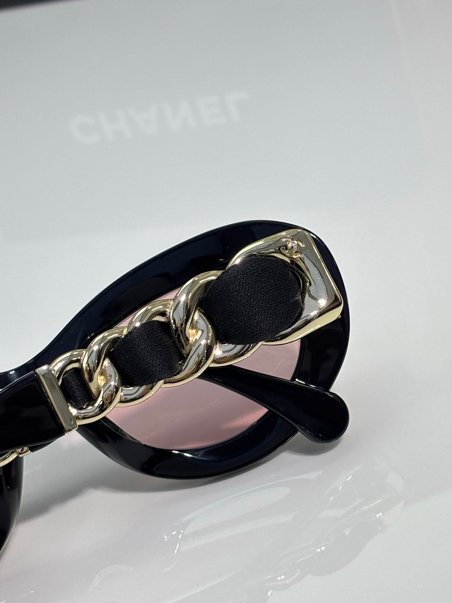 Black sunglasses with gold-tone chain detail and pink-tinted lens