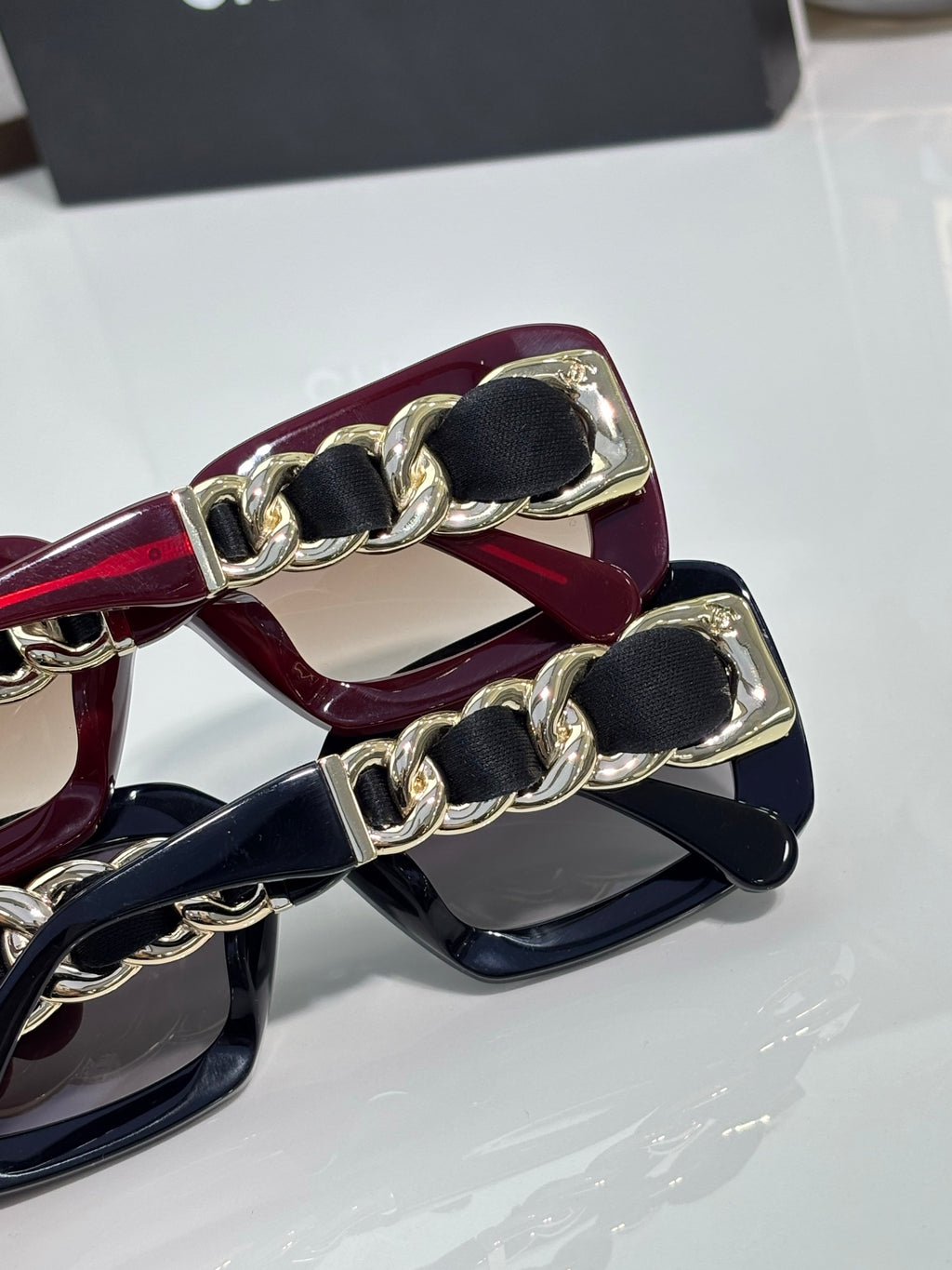 Gold-link chain detail on maroon sunglasses, showing hinge and frame edge