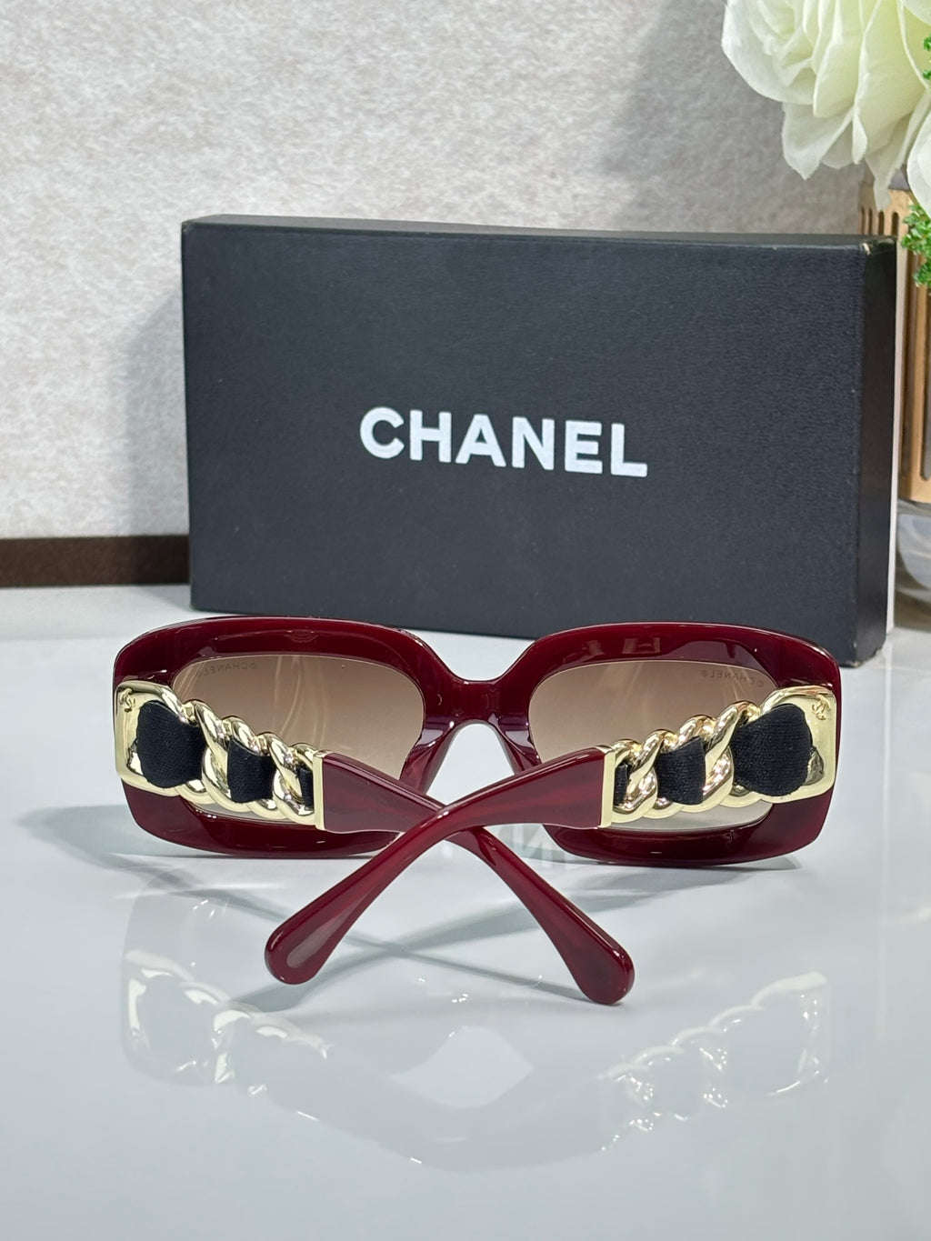 Burgundy sunglasses with gold chain detail on the sides and tinted lenses