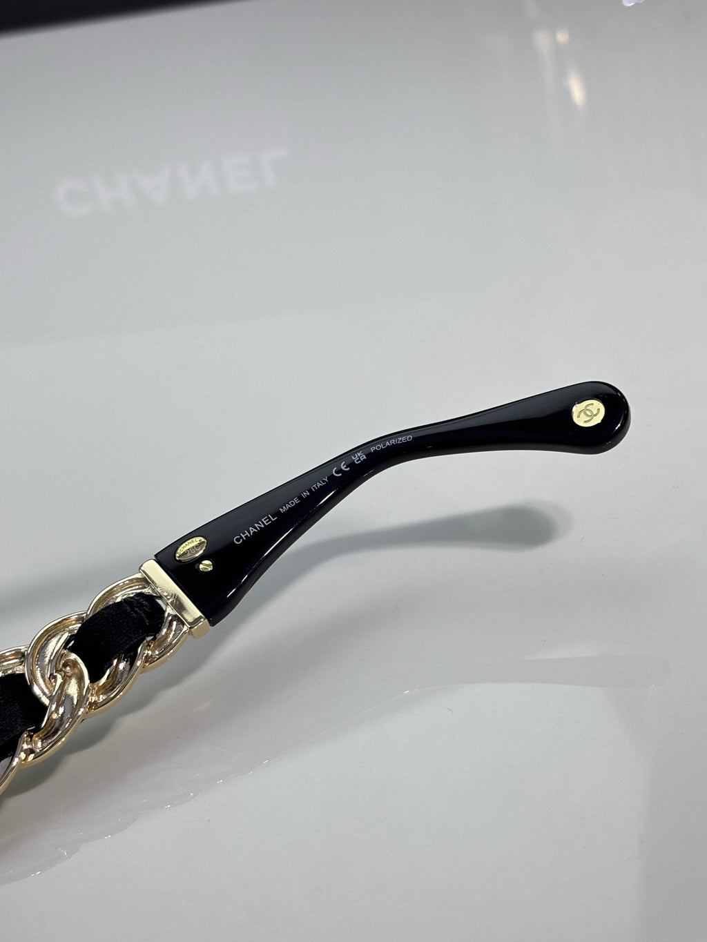 Maroon-black sunglasses temple with gold chain accent and CHANEL branding