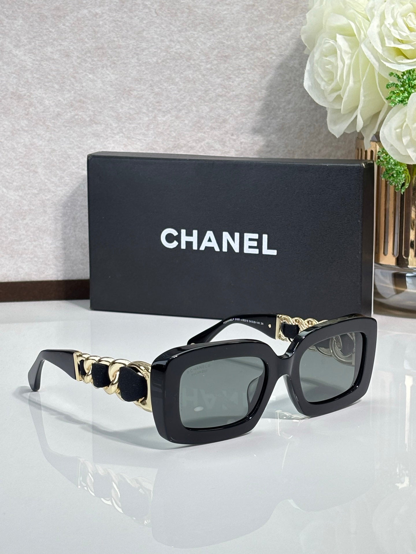 Black square sunglasses with gold chain temples and tinted lenses